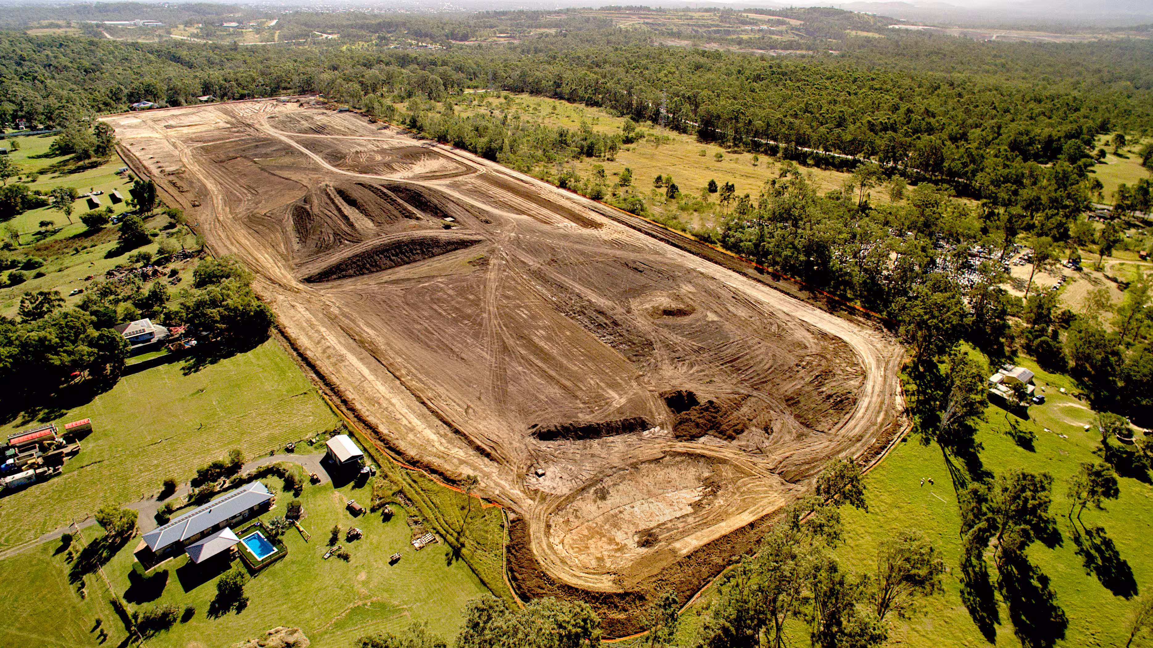 Aerial view of a large construction site showing cleared, leveled land with earthworks and heavy machinery in a rural, forested setting.