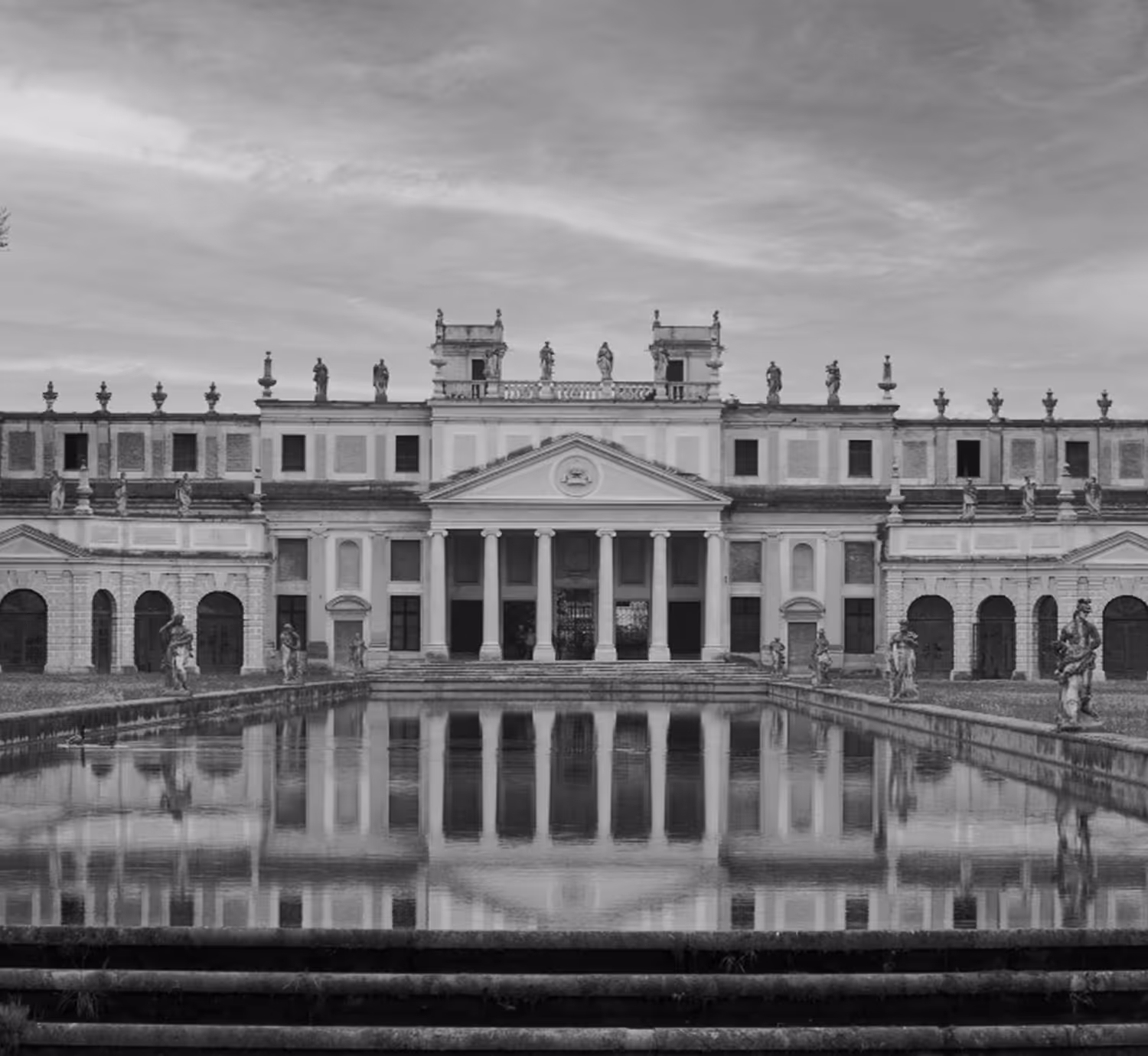 Historic neoclassical building with statues lining the roof and a reflecting pool in front.