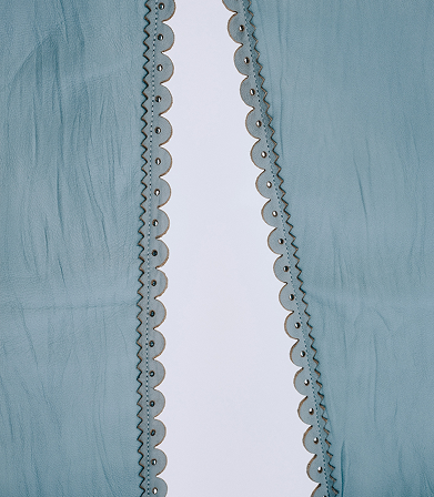 Close-up of light blue fabric with a central vertical cutout bordered by scalloped edges and decorative stitching.