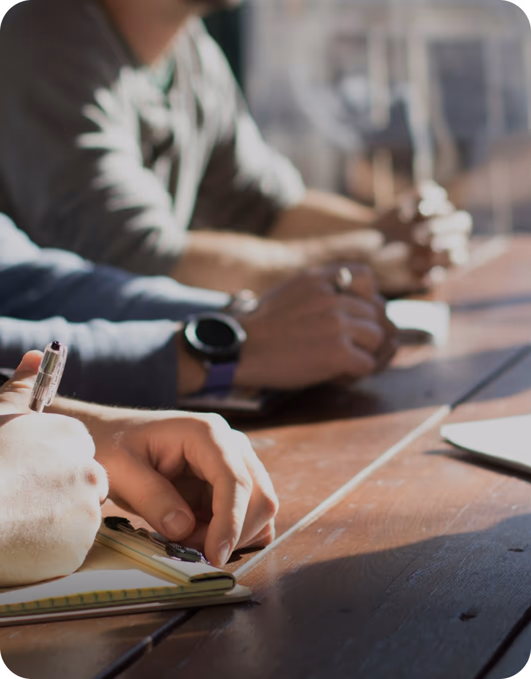 Close-up of hands writing on notepads during a meeting at a wooden table with natural light.