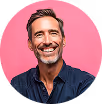 Smiling middle-aged man with gray hair wearing a dark blue shirt against a pink background.