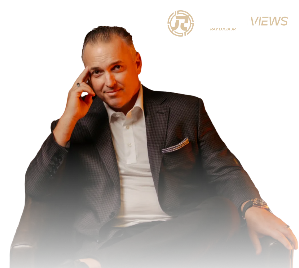 Man in a dark checkered blazer and white shirt sitting on a leather chair with a thoughtful expression.