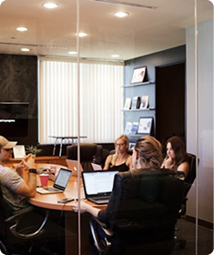 Four people in a modern office meeting room discussing with laptops and documents.