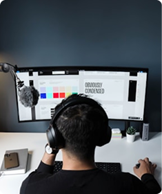 Person wearing headphones working at desk with ultra-wide curved monitor and white desk setup.
