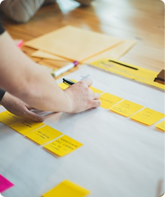 Person organizing yellow sticky notes on a table with papers and a laptop nearby.
