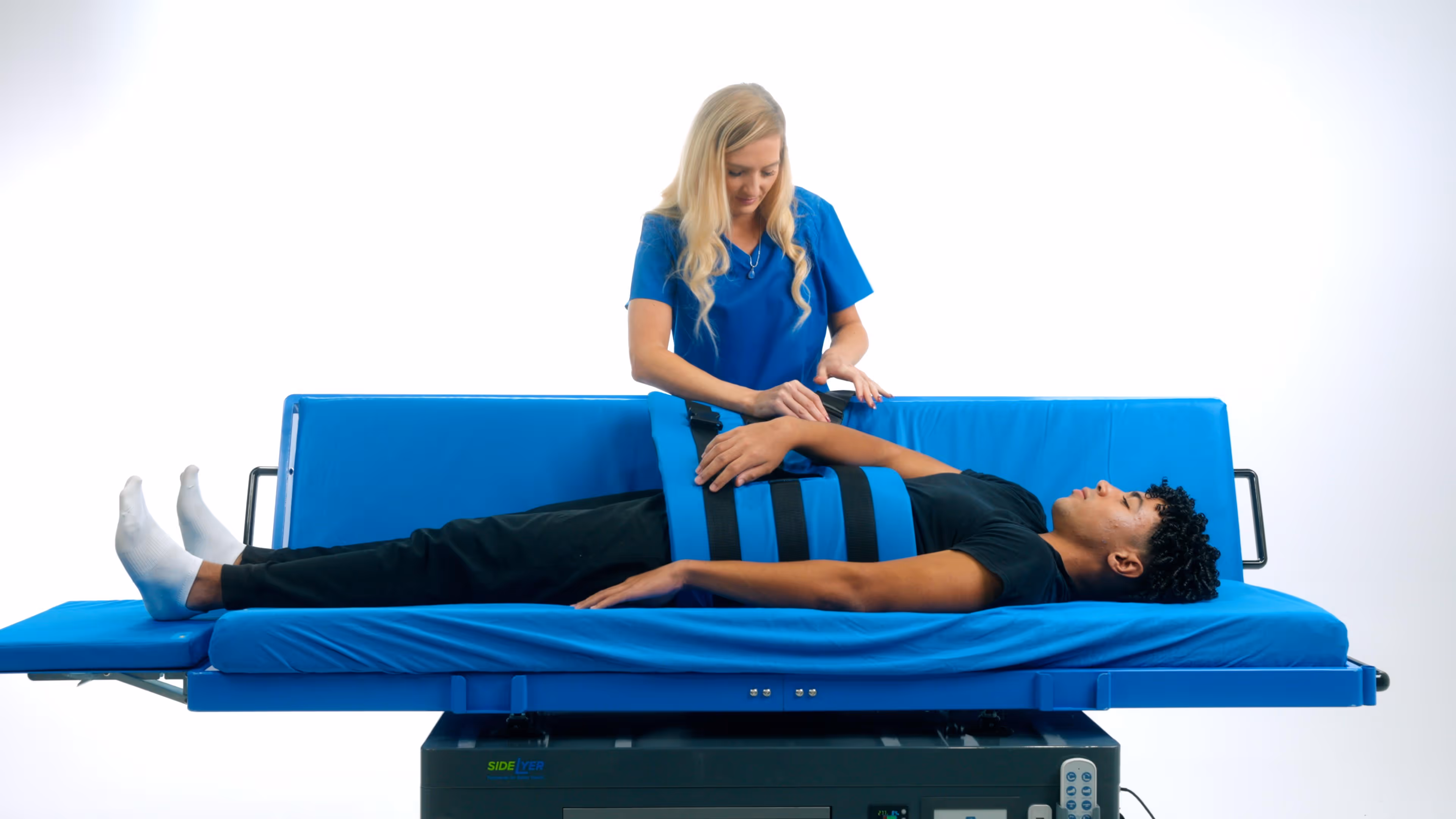 Medical professional securing a strap around a young man lying on a blue hospital bed.