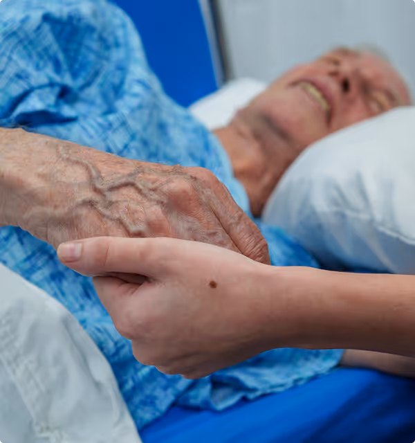Close-up of a young adult holding the hand of an elderly person lying in a hospital bed.