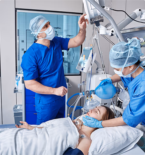 Medical team in blue scrubs and masks providing anesthesia and monitoring a patient lying unconscious on a hospital bed.