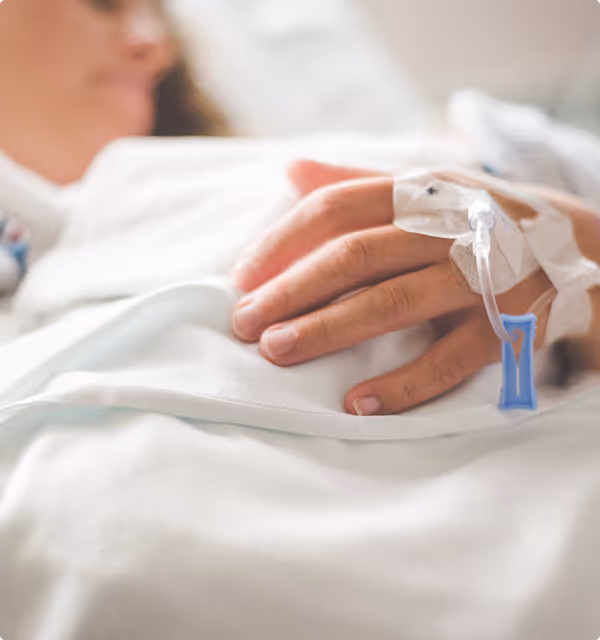 Close-up of a patient's hand with an intravenous (IV) line inserted, resting on a white hospital blanket.