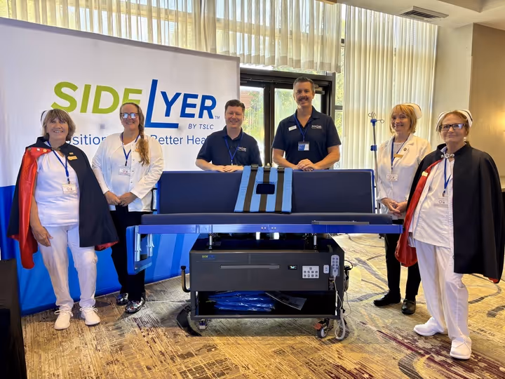 Six medical professionals standing behind a Lateral Positioner device with a SIDE LYER banner in the background.