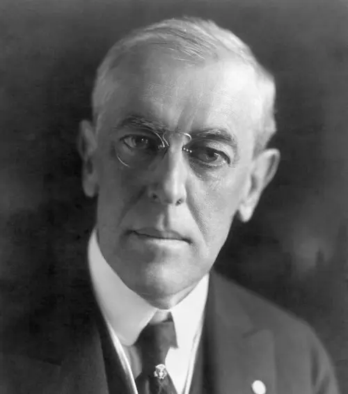 Black and white portrait of an older man with round glasses wearing a suit and tie.
