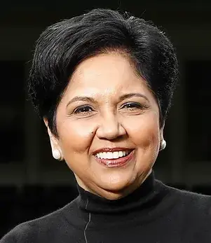 Close-up portrait of a smiling woman with short black hair wearing pearl earrings and a black turtleneck.