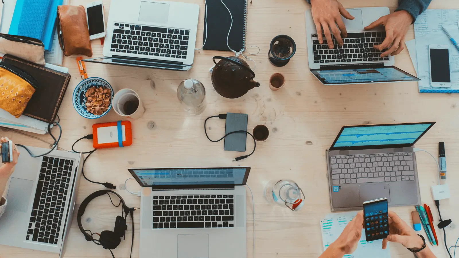 Table with multiple computers and people sitting in front of them. 