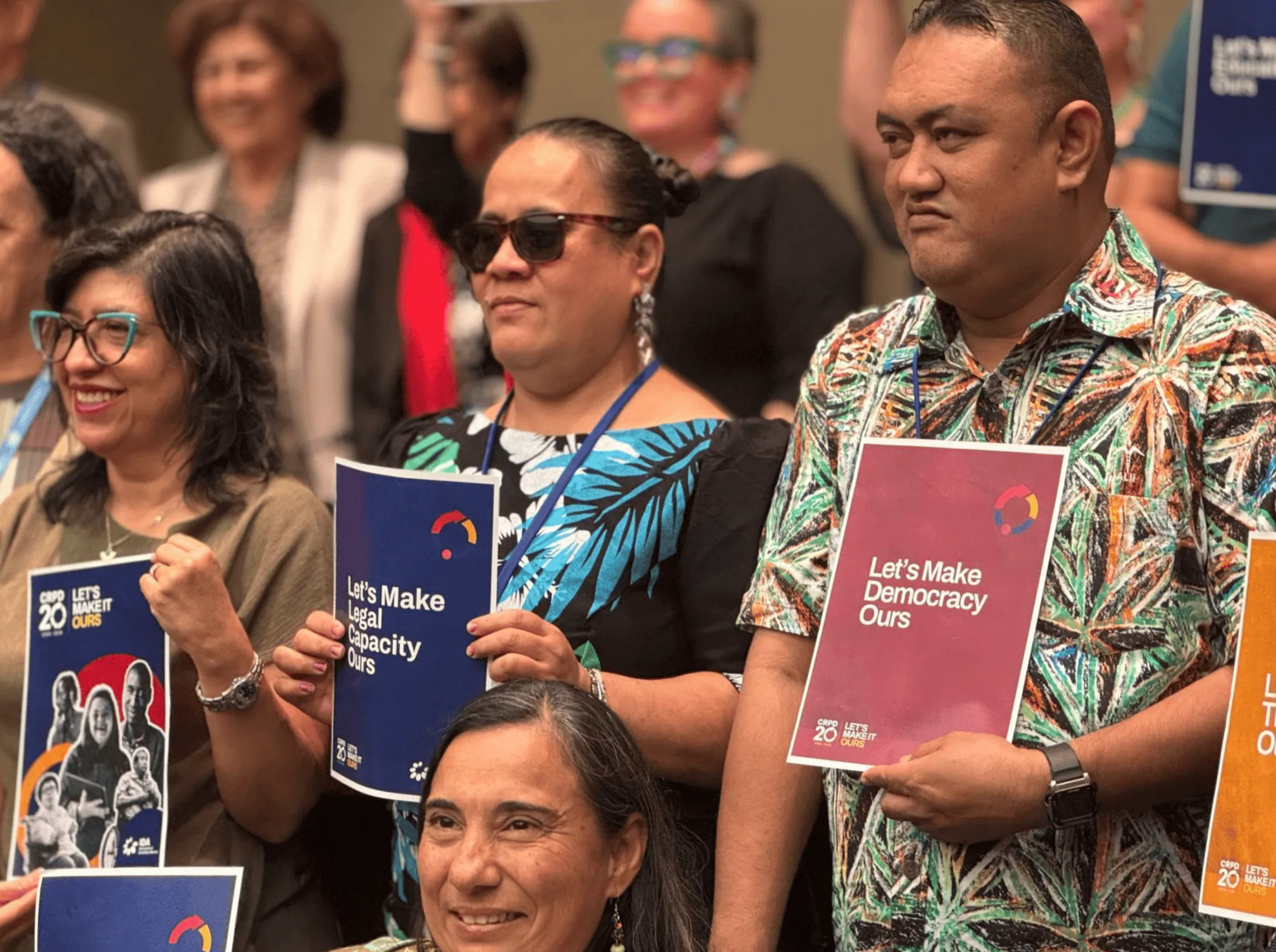 A group of persons with disabilities holding signs of the Let's Make It Ours campaign an te civil society forum