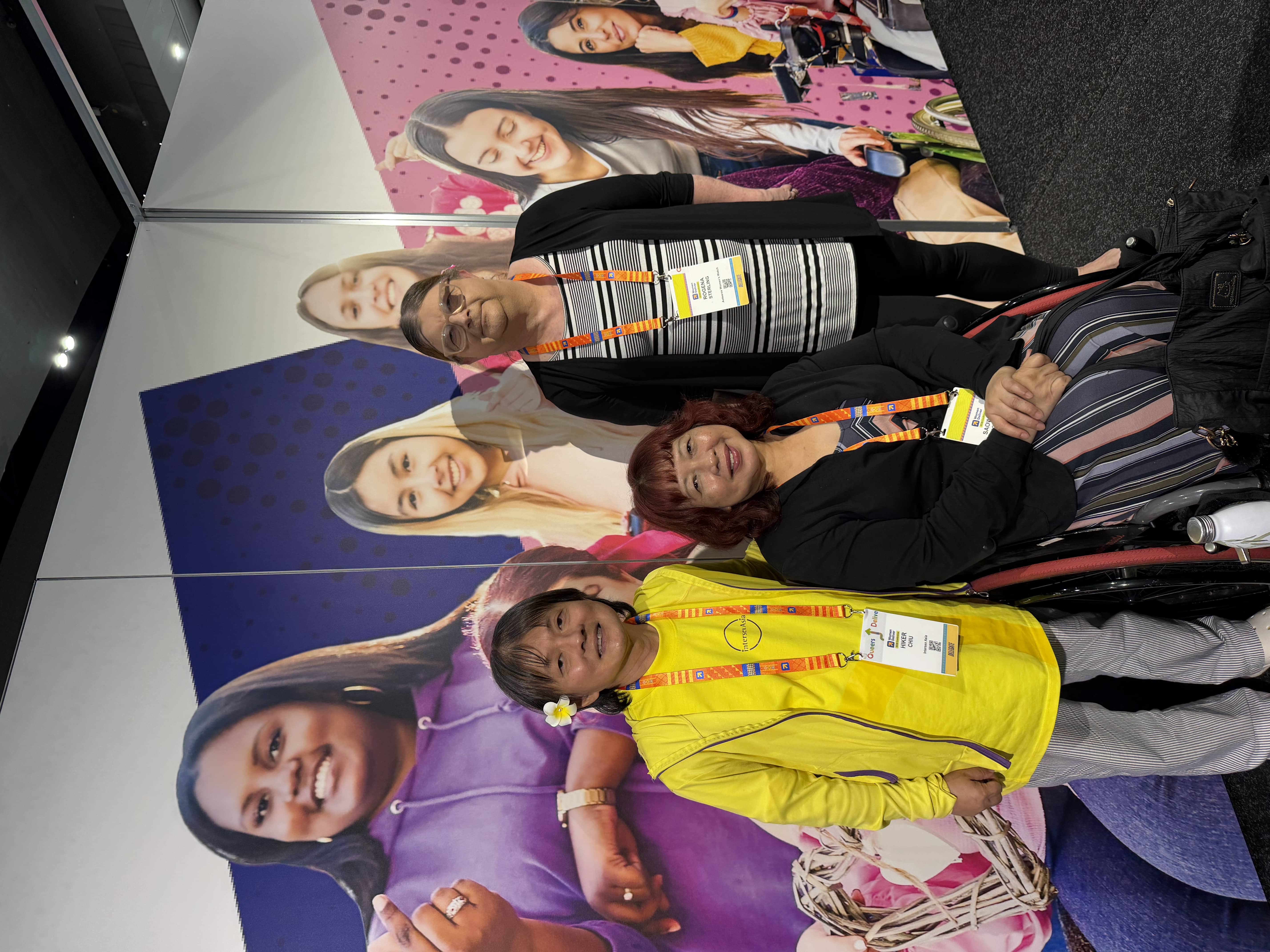 Three women at IDA Women Deliver stand. There is a wheelchair user in the middle.