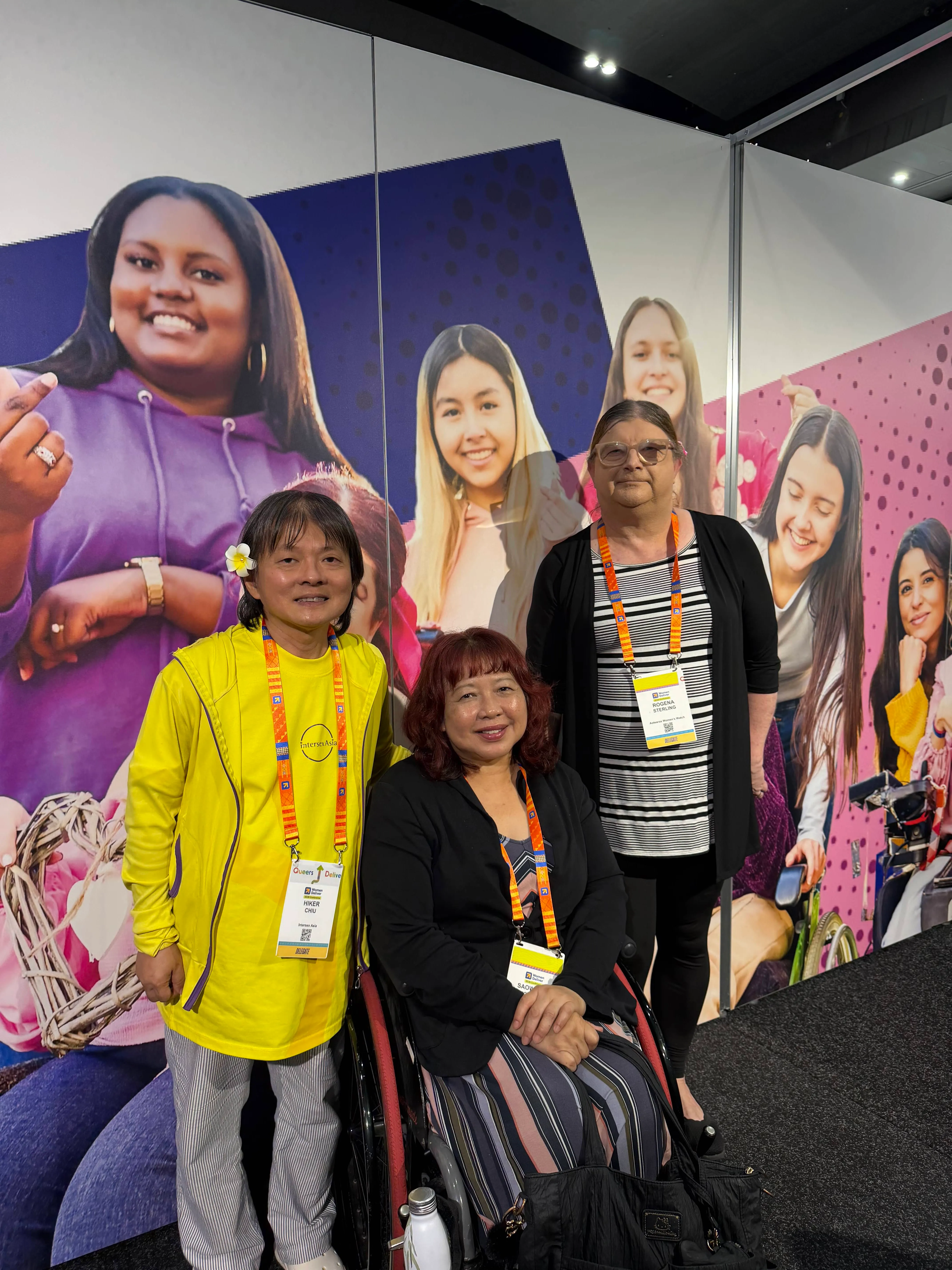 Three women at IDA Women Deliver stand. There is a wheelchair user in the middle.