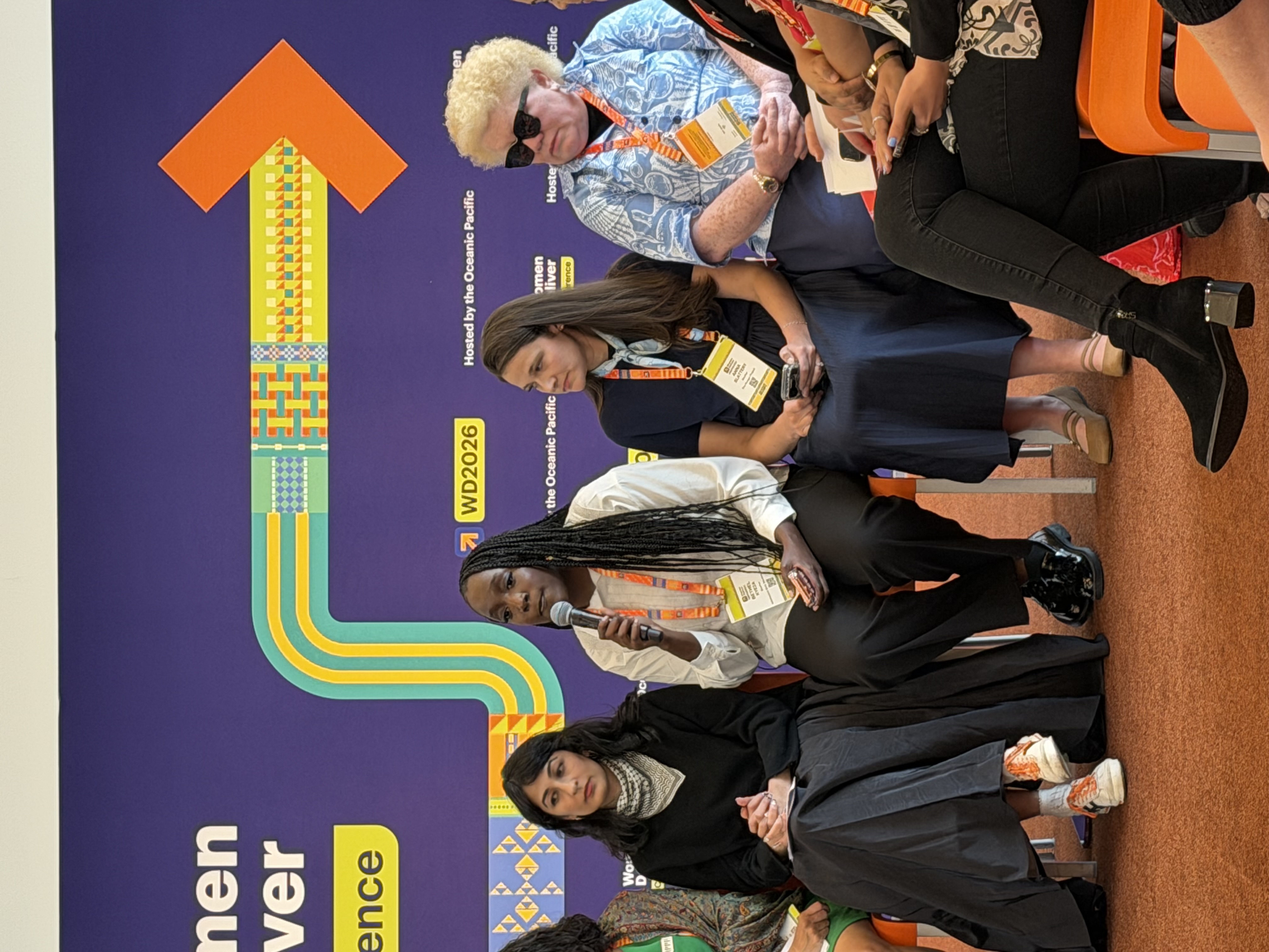 Women at the press conference at Women Deliver. There is a woman speaking with a mic on her hand