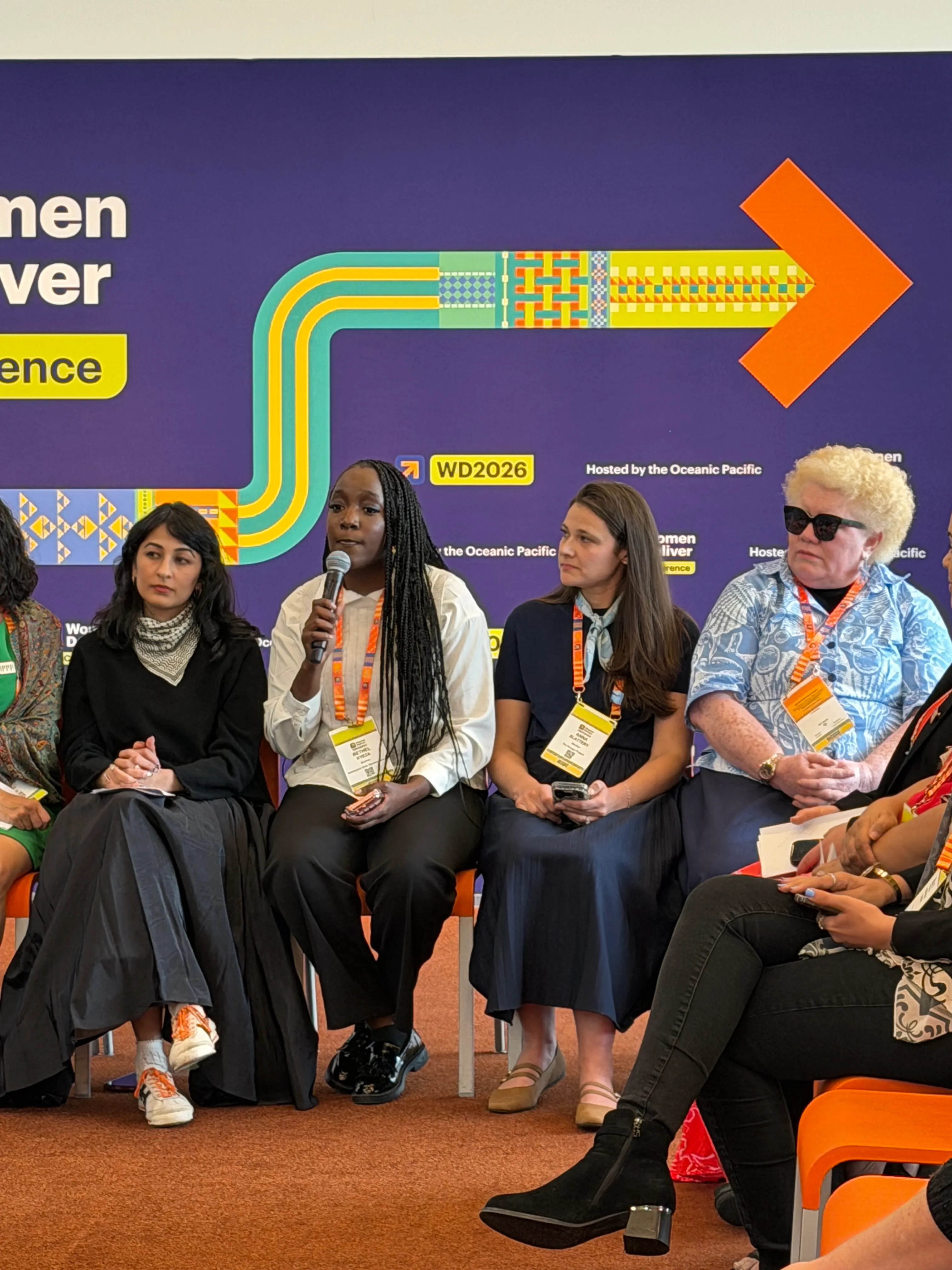 Women at the press conference at Women Deliver. There is a woman speaking with a mic on her hand