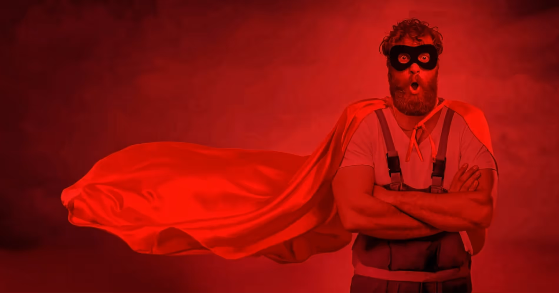 Man with a beard wearing a superhero mask and red cape, arms crossed and making a surprised face.