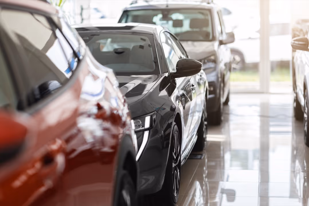 Row of new luxury cars parked indoors in a showroom with shiny tiled floor.