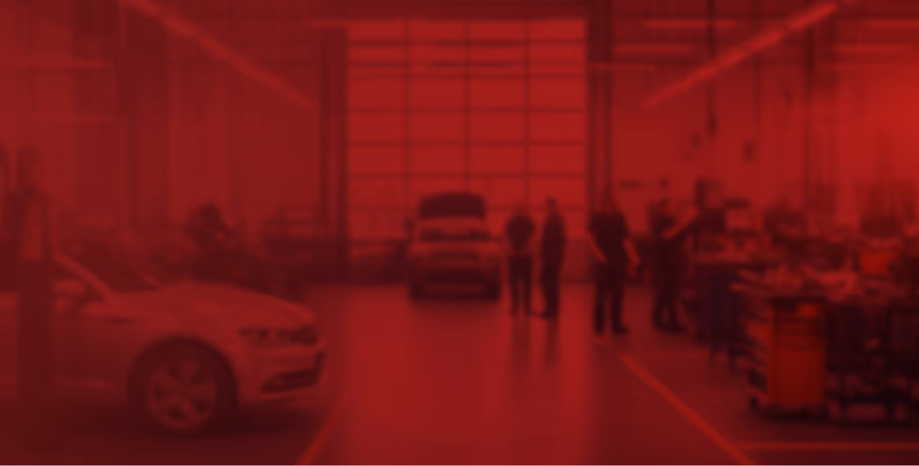 Blurry image of a car workshop with two cars and several people standing and working inside.