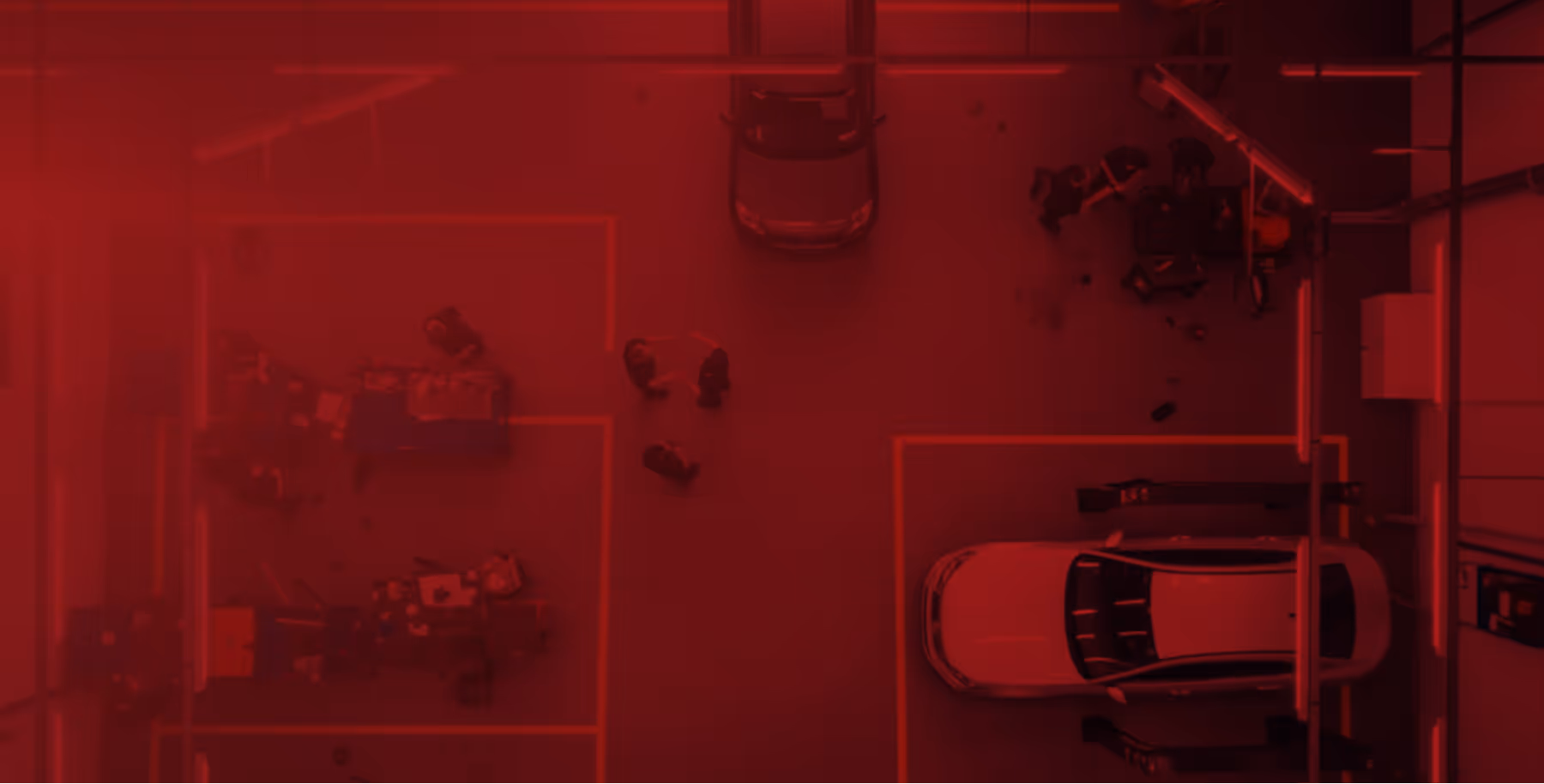 Overhead view of a car workshop with two cars in service bays and several workers around them.