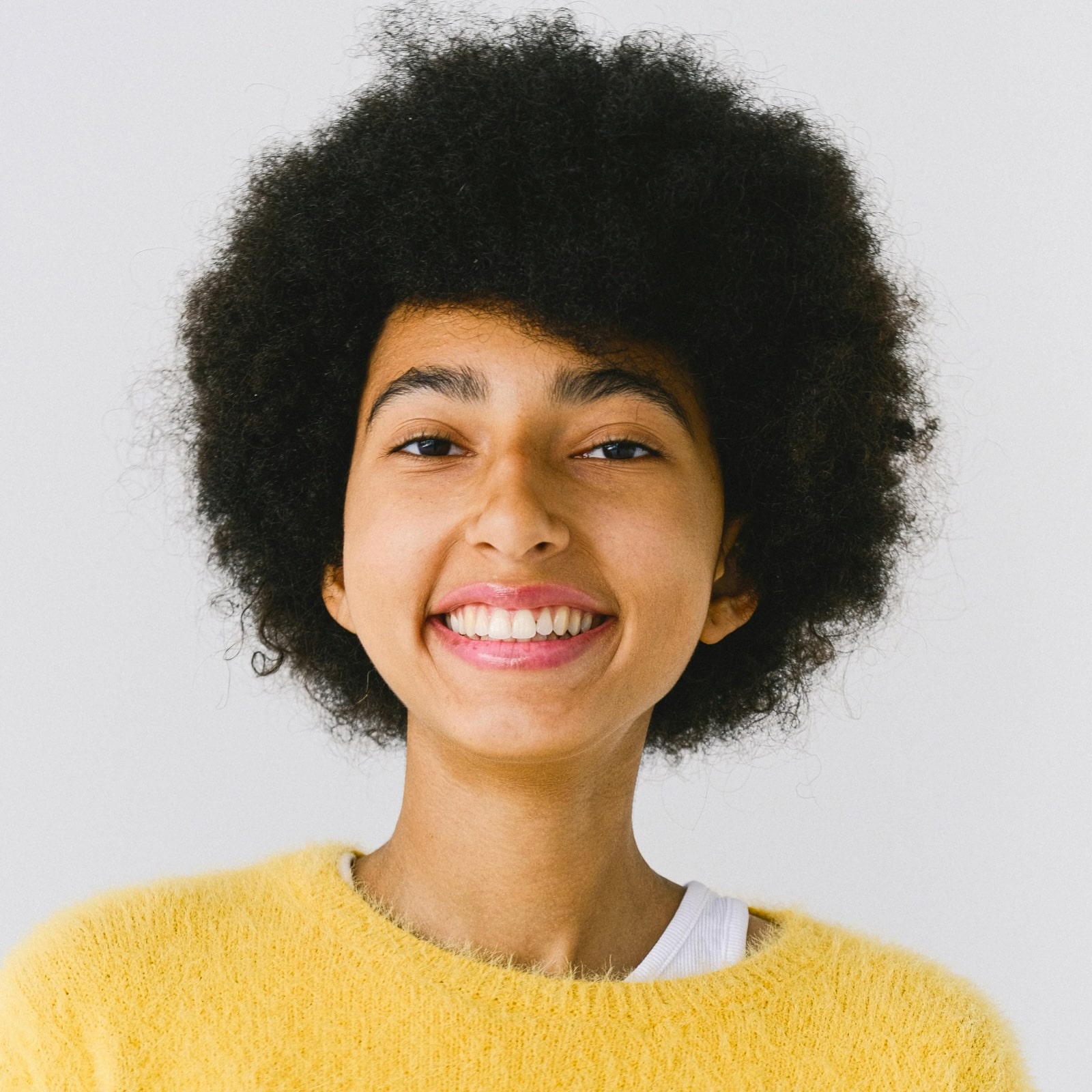 Smiling young woman with afro hairstyle wearing a yellow fuzzy sweater and white top.