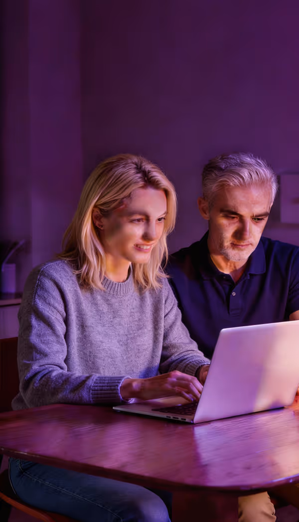 Två personer arbetar tillsammans på en bärbar dator i lila belysning