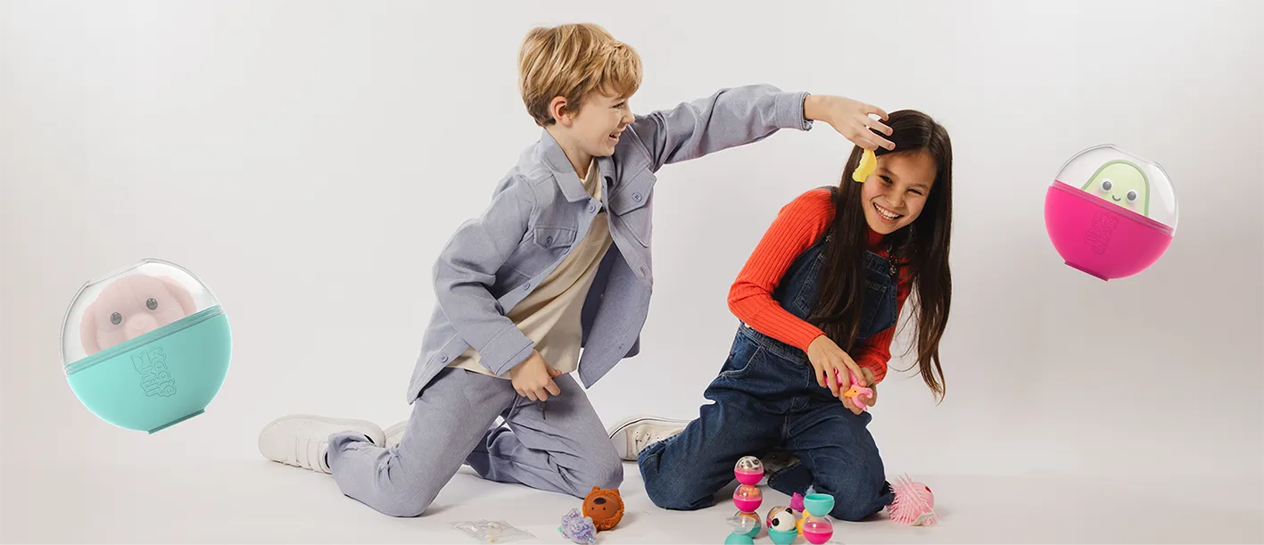 A boy and a girl happily playing with colorful toys on the floor, the boy holding a yellow toy above the girl's head.
