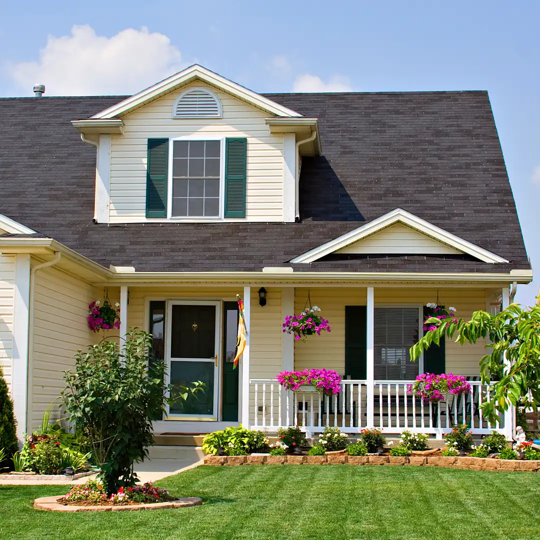 Beige home exterior with covered front porch, dark shingle roof, and landscaped yard