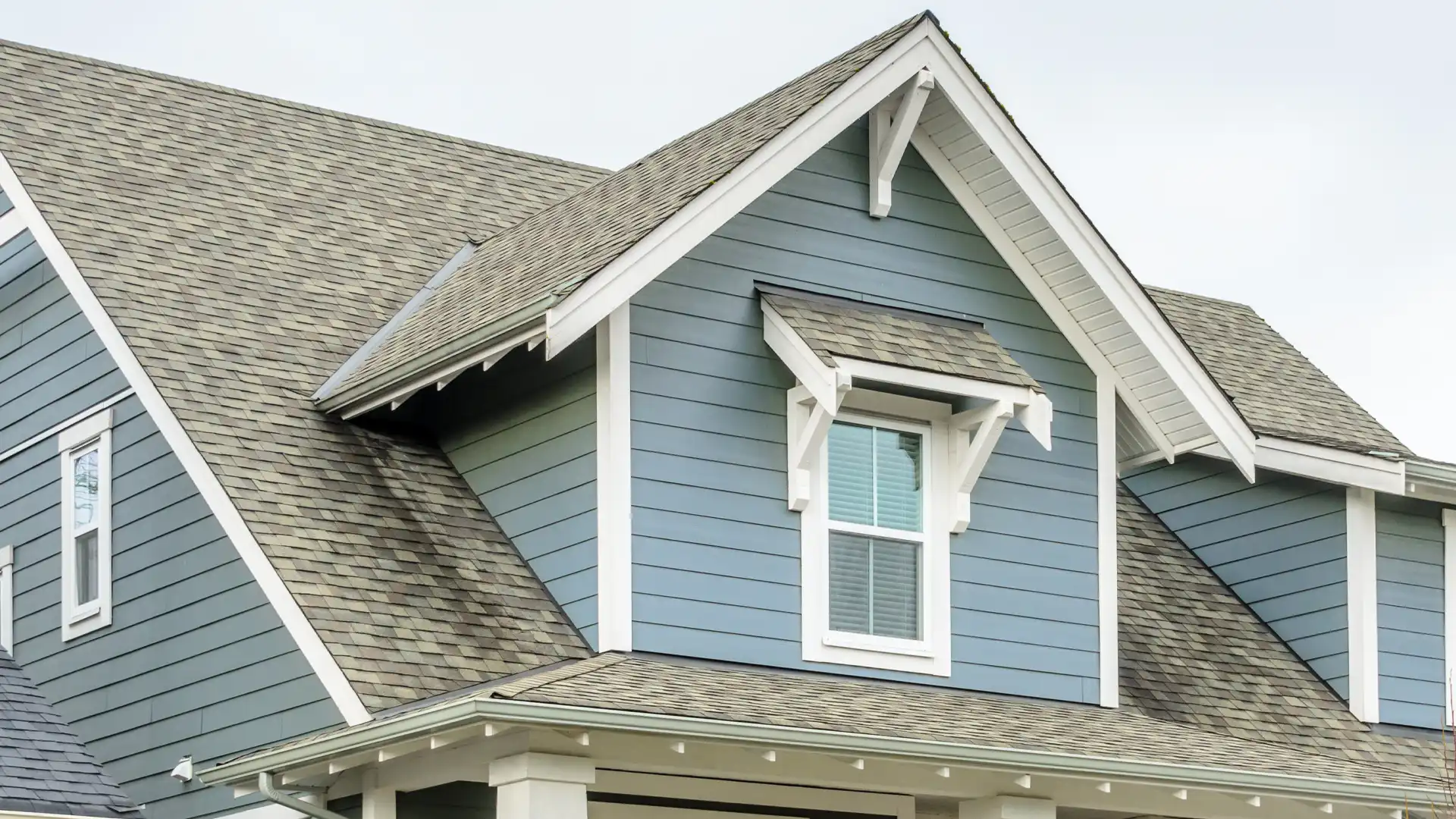 Blue home exterior with gray asphalt shingle roof, white trim, and decorative gable brackets