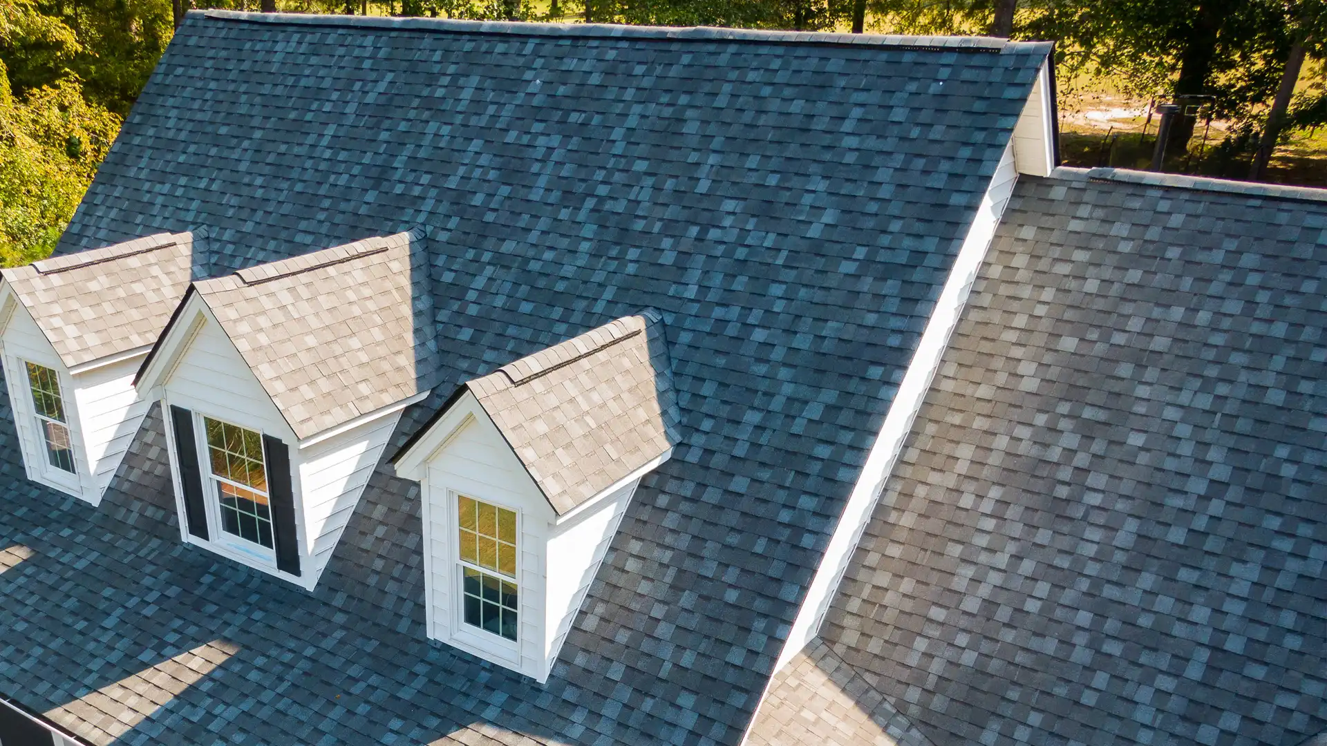 Close-up of asphalt shingle roof with two dormer windows and contrasting shingle colors