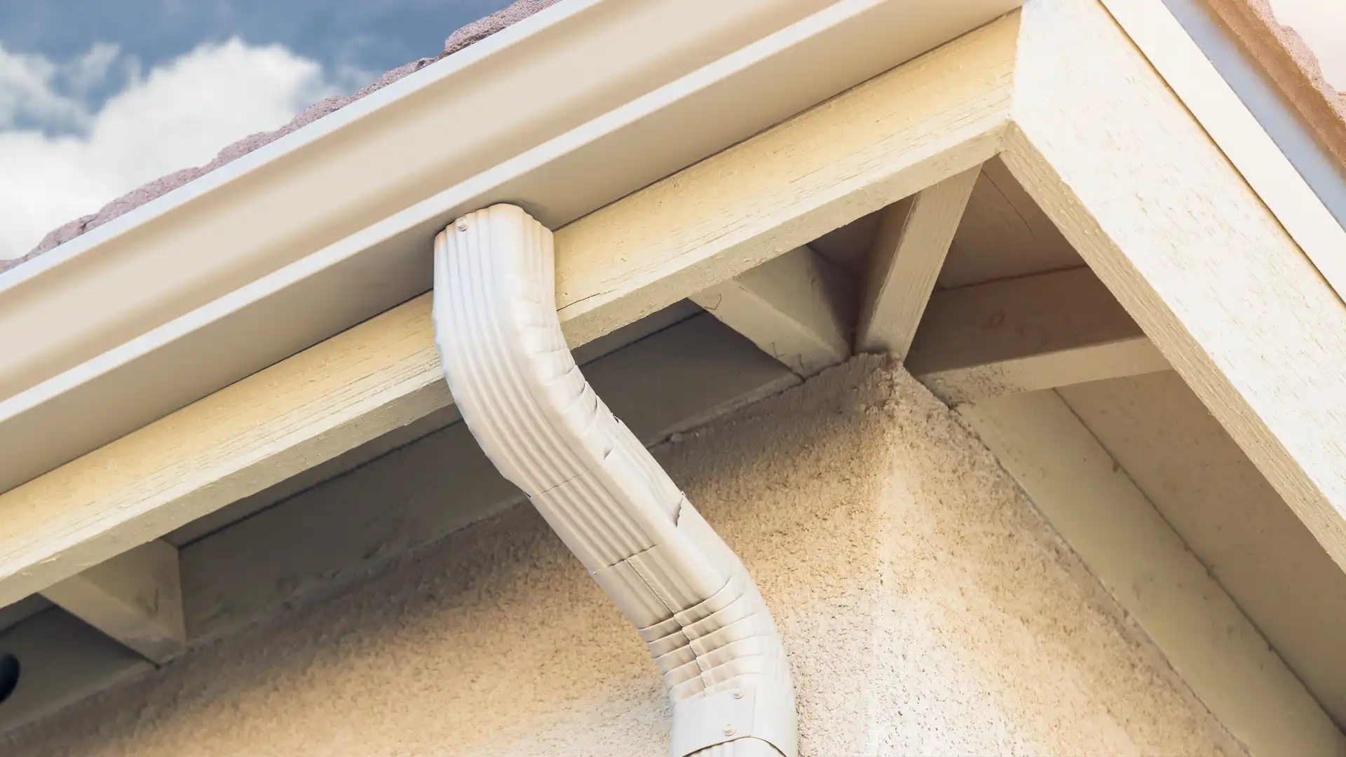 White downspout and gutter system installed along a roof edge on a stucco exterior