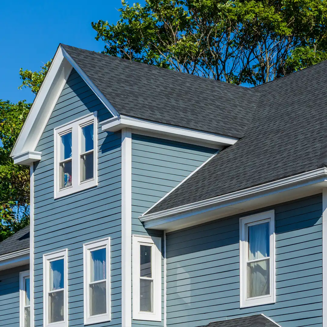 Blue home exterior with dark asphalt shingle roof and white-trimmed windows on a sunny day