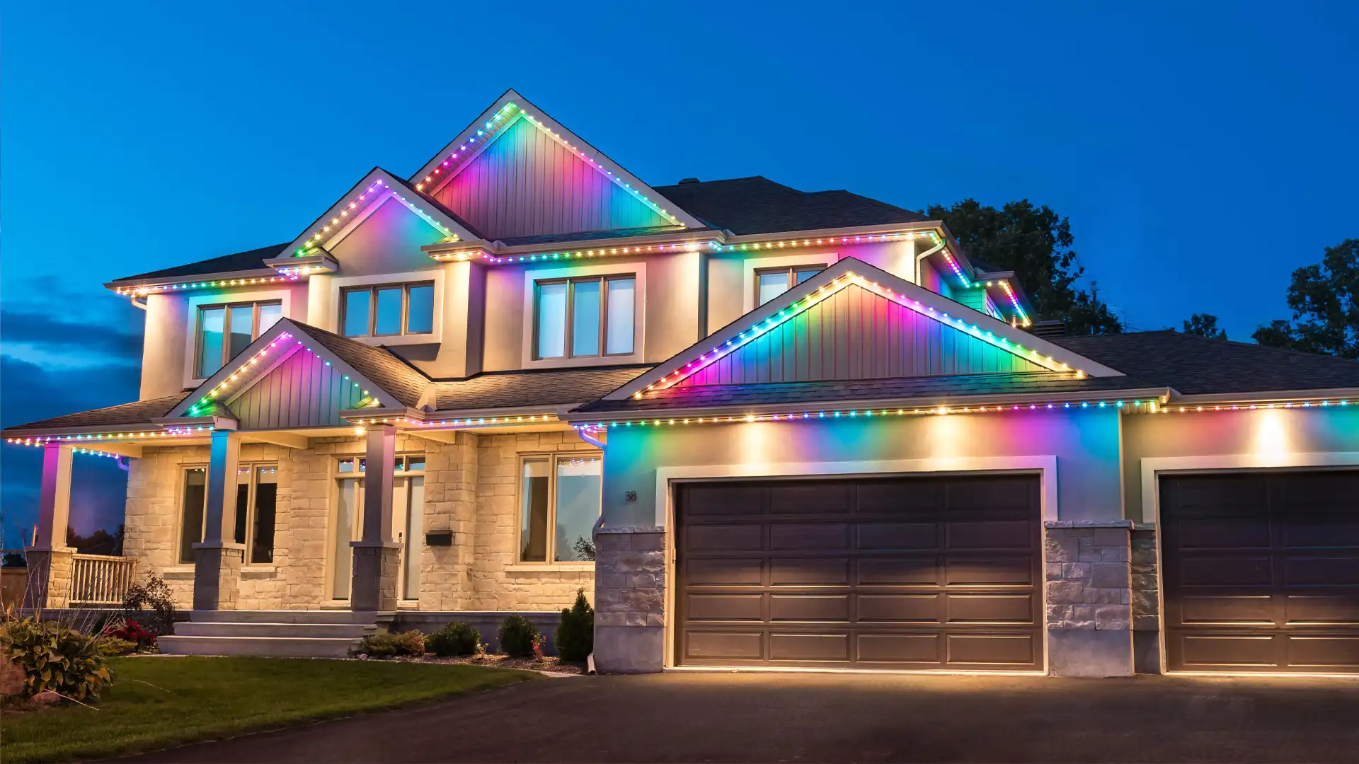 Two-story home at night with colorful permanent LED holiday lights installed along the roofline