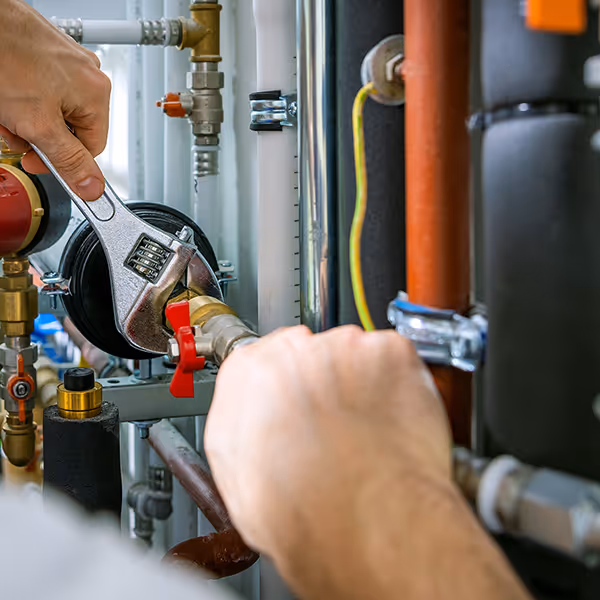 Person using an adjustable wrench to tighten a valve on a heating system pipe.