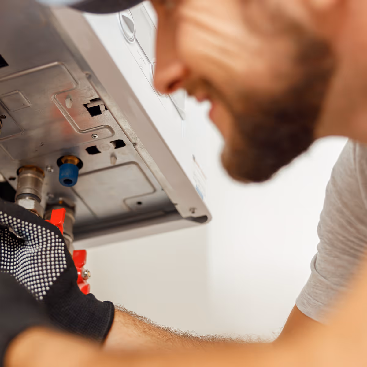 Man wearing gloves inspecting or repairing the underside of an appliance or boiler.