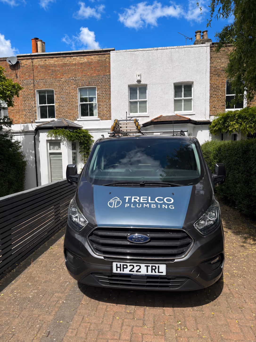 Front view of a Ford van with Trelco Plumbing logo parked on a driveway in front of a brick house.