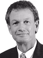 Black and white headshot of a man with short curly hair wearing a suit and tie, smiling slightly.