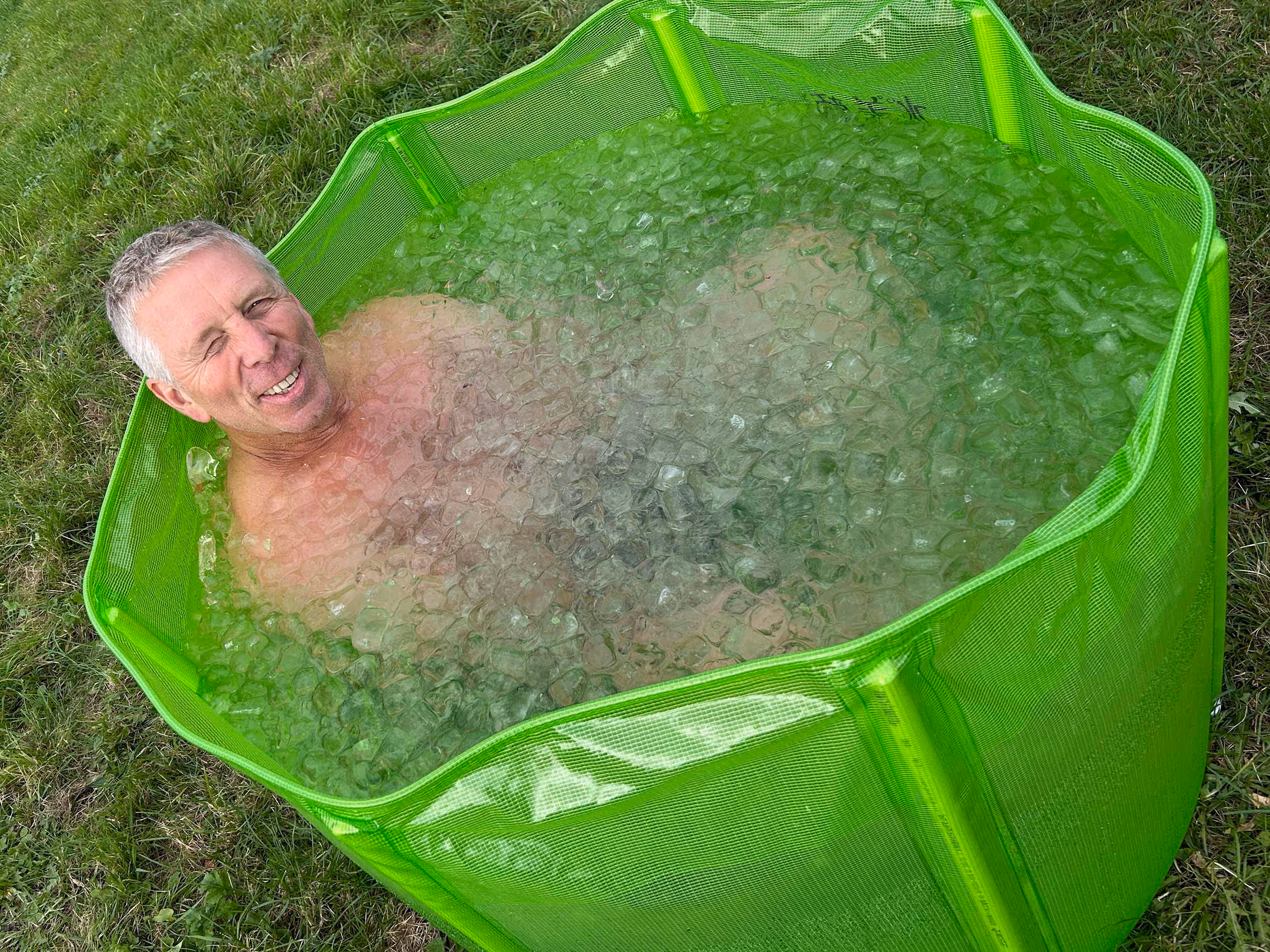 Homme souriant dans une piscine verte remplie de glace posée sur l'herbe.