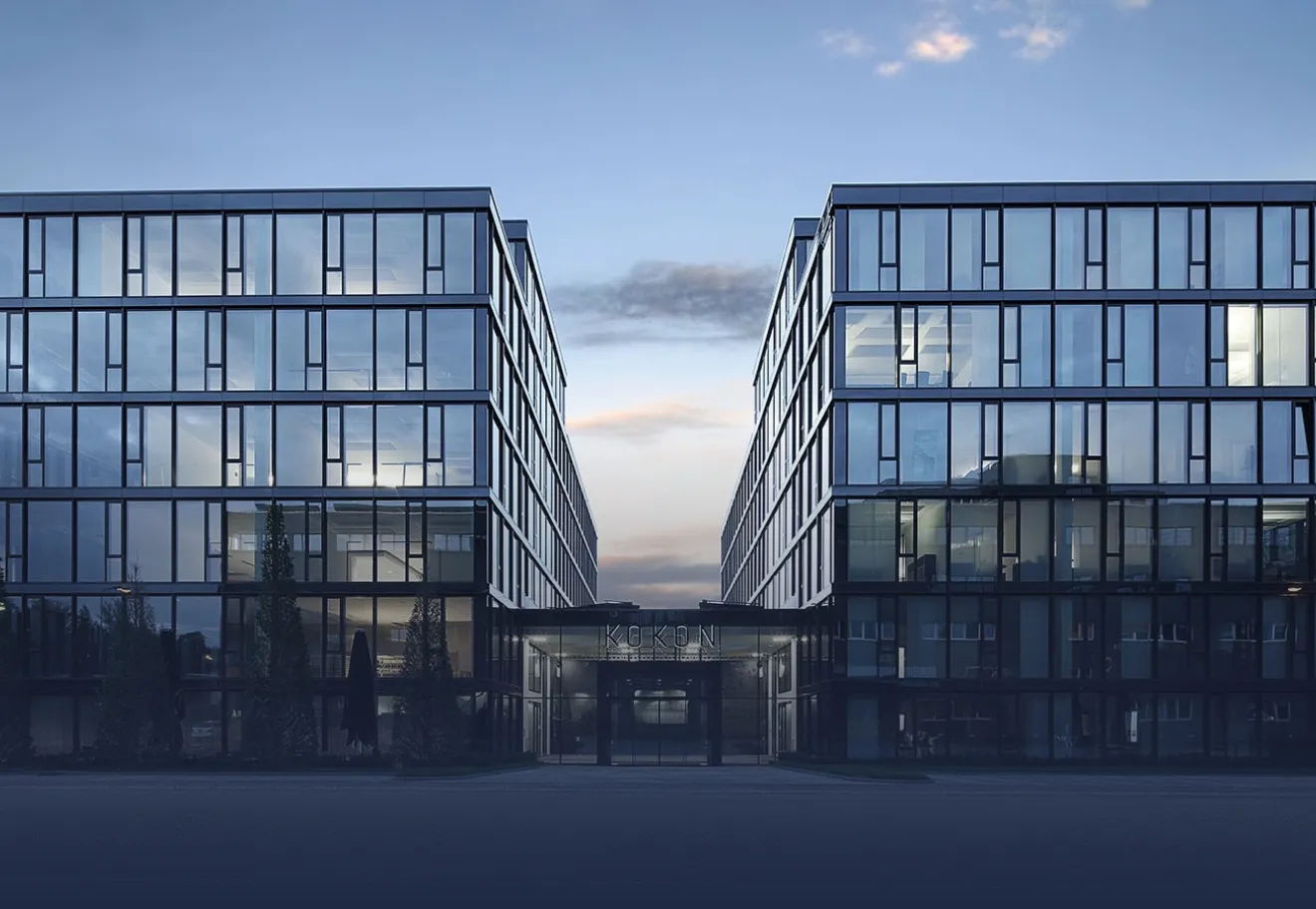 Frau mit langem blondem Haar und kariertem Blazer, die einem Mann gegenübersitzt und lächelt.