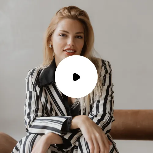 Frau mit langen blonden Haaren und gestreiftem Anzug sitzt entspannt auf einem braunen Sofa.