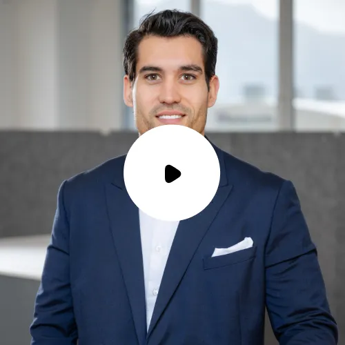 Junger Mann in dunkelblauem Anzug und weißem Hemd lächelt im Büro.