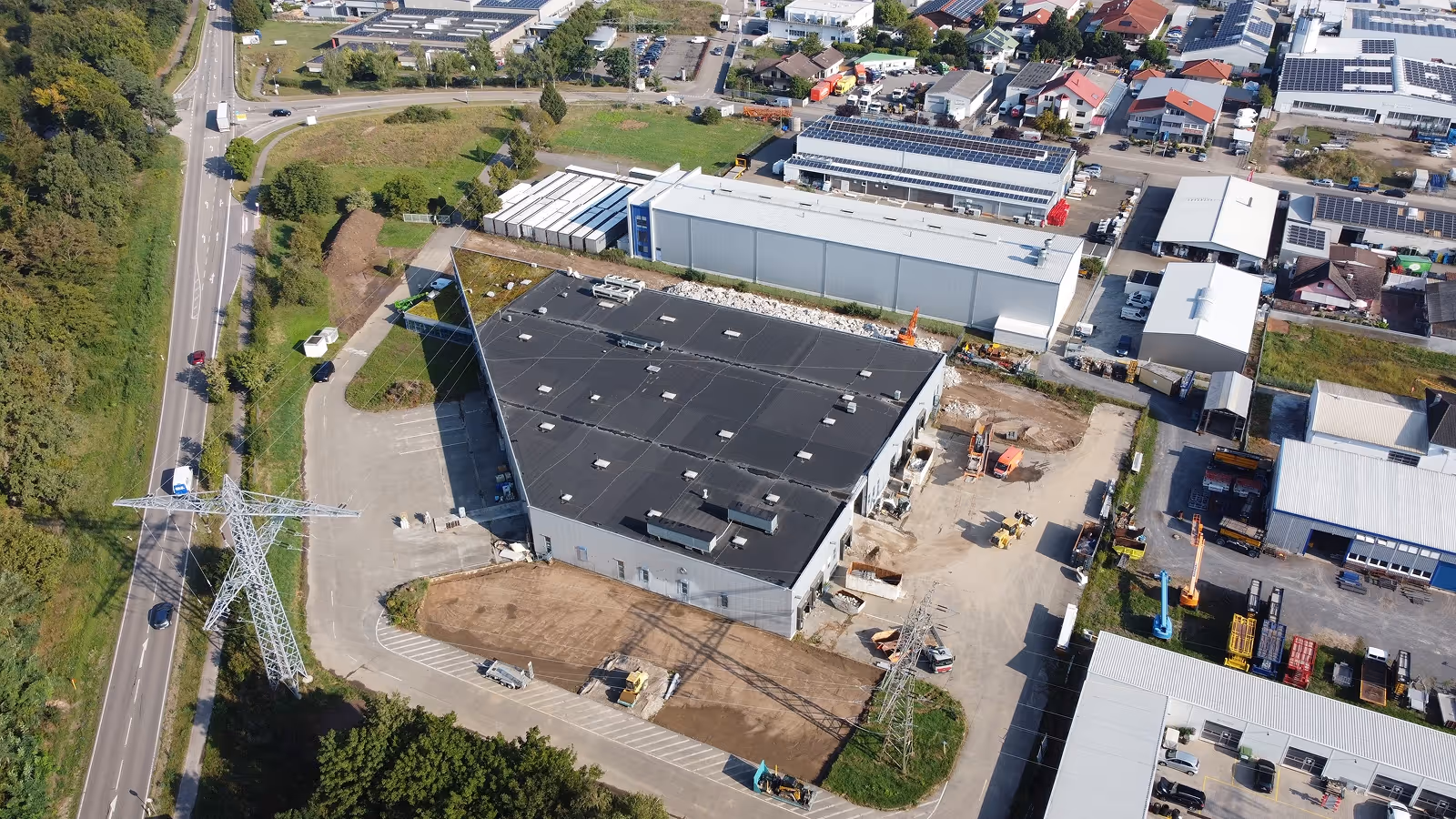 Luftaufnahme eines Industriegebiets mit einem großen Lagerhaus, Straßen und Strommasten.