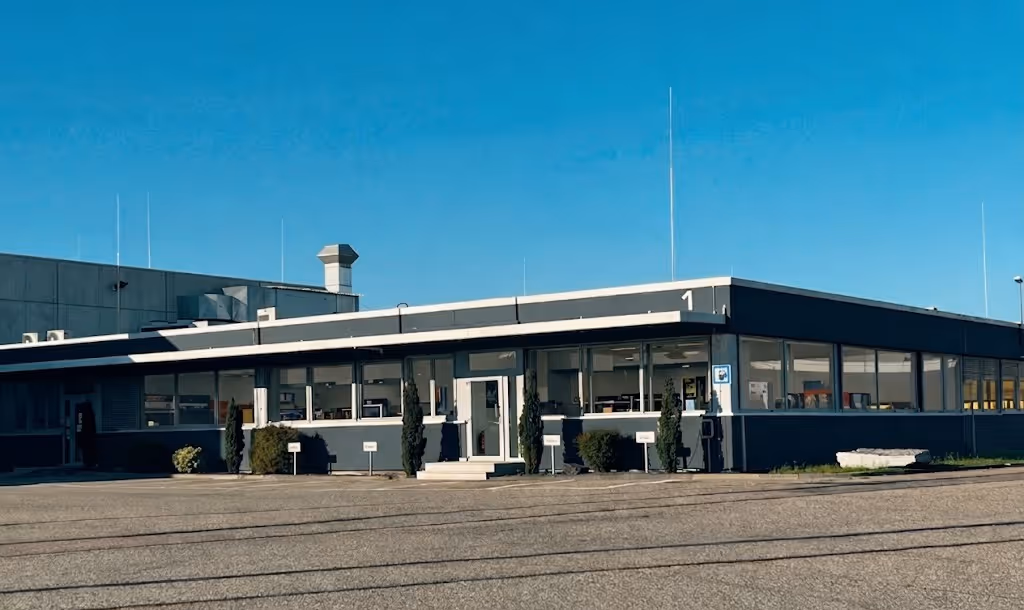 Flaches Bürogebäude mit großen Fenstern und klarem blauem Himmel im Hintergrund.