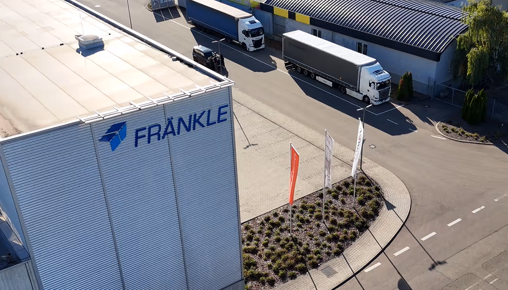 Blick auf fränkles Firmengebäude und Lager mit zwei parkenden Lastwagen auf dem Hof.