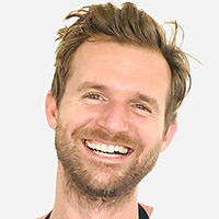 Smiling man with short brown hair and beard on a light background.