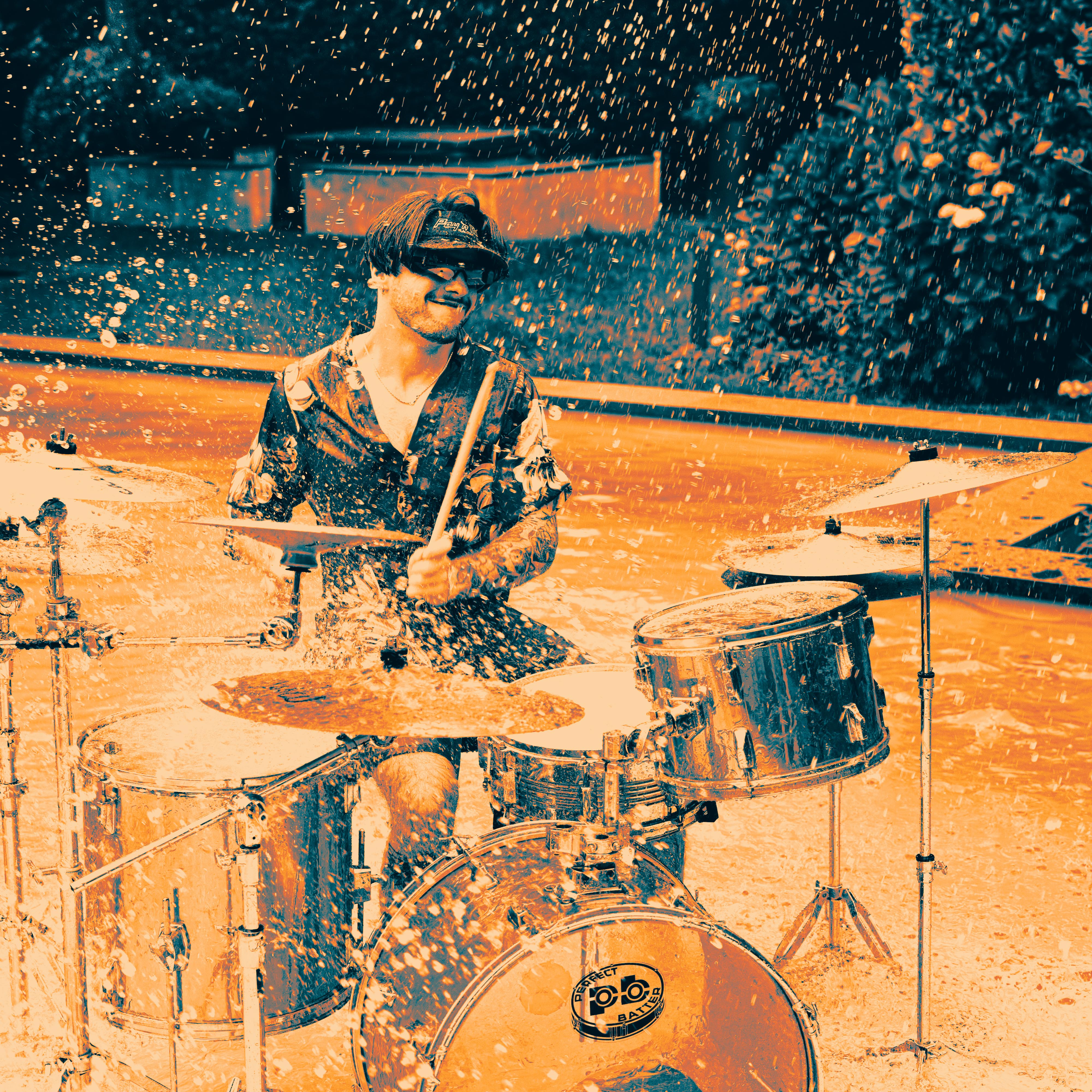 Man playing drums energetically with water splashing around him.