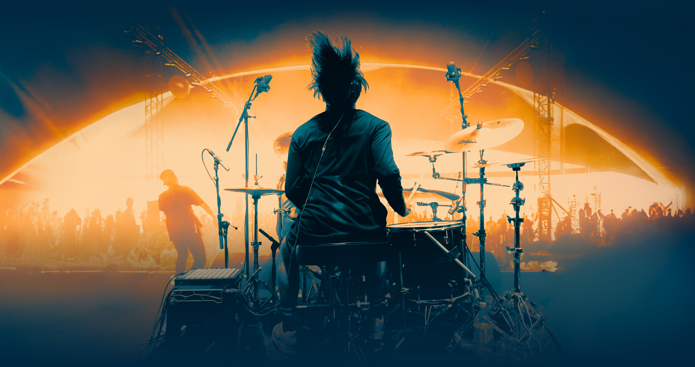 Tattooed drummer playing on stage facing a crowd at a concert.