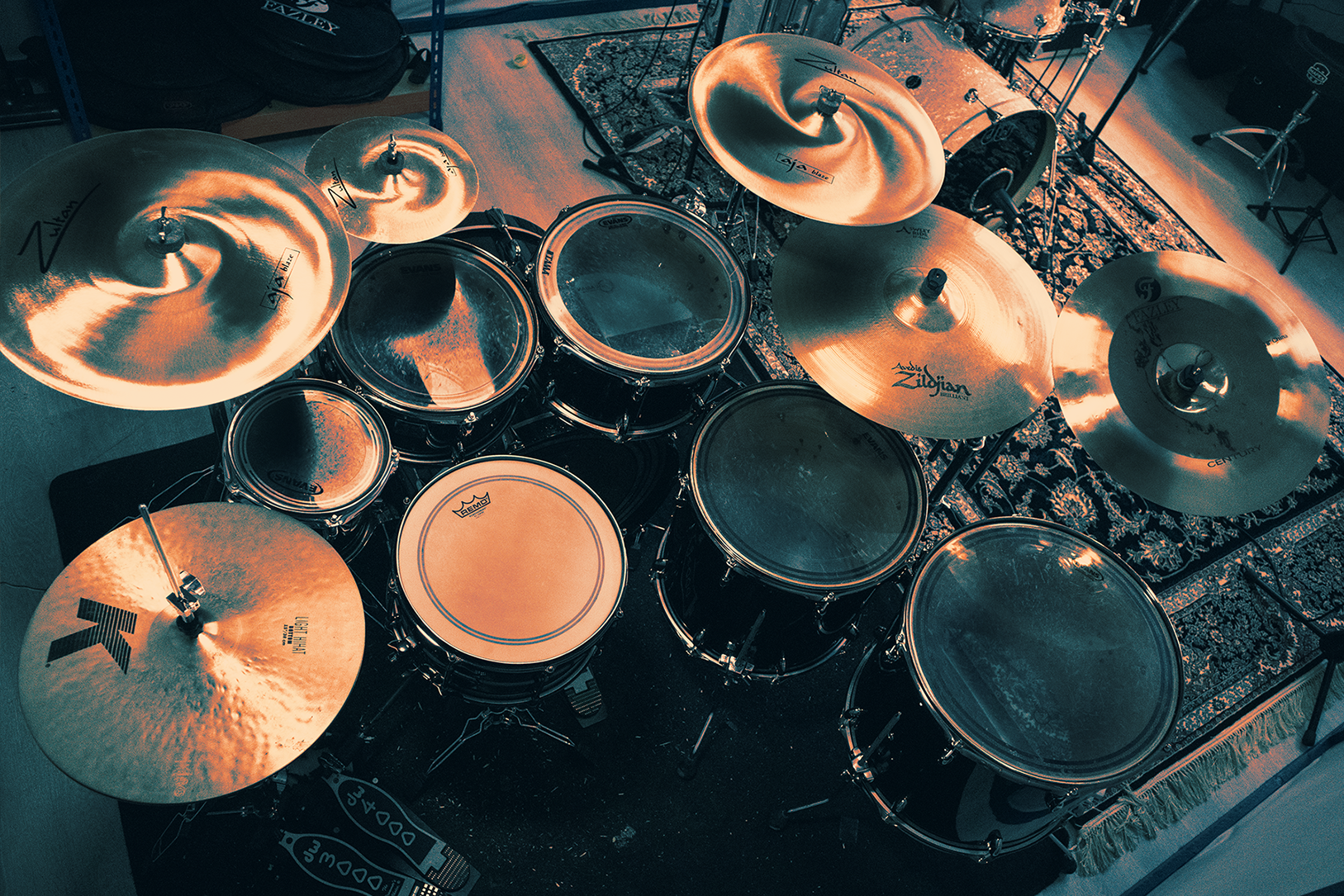 Top-down view of a drum set with multiple cymbals, drums, and pedals on patterned rugs in a music studio.